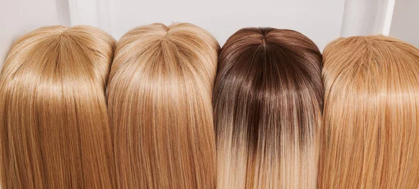 Showcase of natural looking wigs in different shades of blonde fixed on the wig holders in beauty salon. Row of mannequin heads with variation colors fair hair on shelf in wig shop