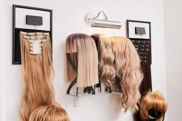 在美容院的金属假发架上展示了不同颜色的天然假发 假发柄架子上有一排不同深浅发色的人体模特头 — 图库照片