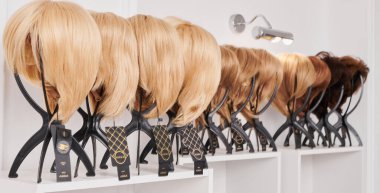 Güzellik salonundaki metal peruk tutuculara sabitlenmiş farklı renklerde doğal görünümlü peruklar. Bir sıra manken kafası ve farklı peruklu saçlar.