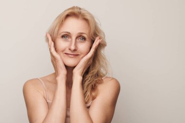 Güzel sarışın, orta yaşlı, gülümseyen, kameraya bakan, yüz portresine dokunan bir kadın. Zarif, olgun bir bayan. Makyajsız. 50 yaşında. Beyaz kadın sağlığı, kozmetoloji, deri araba.