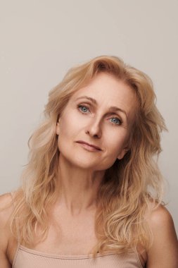 Güzel sarışın, orta yaşlı, gülümseyen bir kadın. Kamera görüntüsü. Zarif, olgun bir bayan. Makyajsız. 50 yaşında. Beyaz kadın sağlığı, kozmetoloji ve cilt bakımı konusunda izole edilmiş.