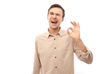 Genç adamın portresi, beyaz arka planda izole edilmiş parmaklarla tamam işareti gösteriyor. Başarılı kariyer, onaylanmış konsept