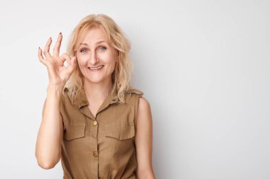 Yetişkin bir kadının portresi beyaz arka planda izole edilmiş parmakları ile tamam işareti gösteriyor. Başarılı bir kariyer, kabul görmüş bir kavram.