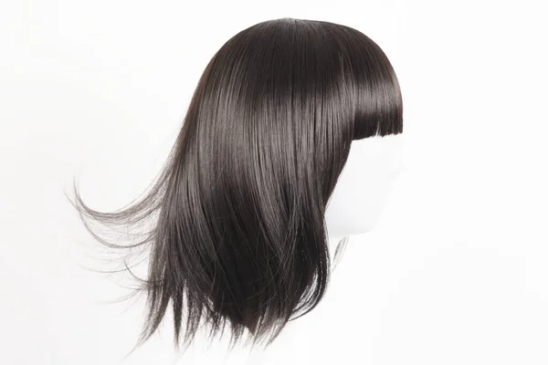 Natural looking black wig on white mannequin head. Medium length straight hair with bangs on the metal wig holder isolated on white background, side view