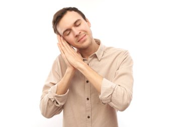 Stüdyo portresi genç adam avuçlarını kafasının altına koyup beyaz arka planda izole bir şekilde uyuyor numarası yaptı.