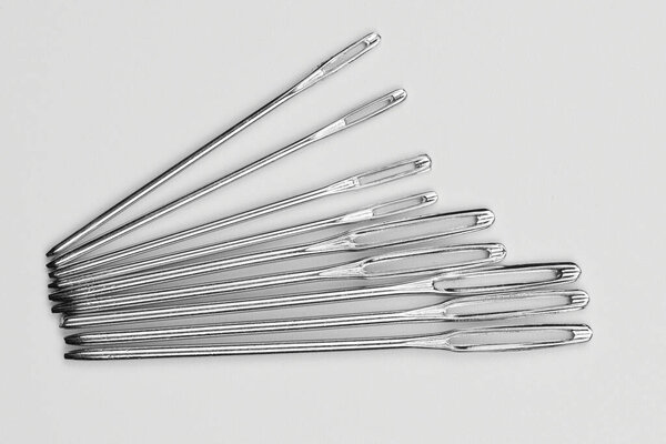 Set of silver sewing needles of different sizes isolated on white background top view, flat lay
