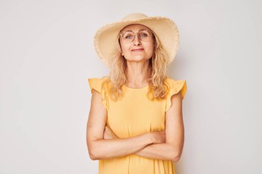 Sarı elbiseli, gözlüklü ve hasır şapkalı mutlu sarışın bir kadının portresi beyaz stüdyo arka planında neşeli bir şekilde sırıtıyordu. Tatil ve seyahat kavramı