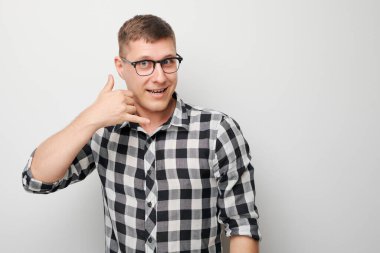 Genç bir adamın portresi, birini arıyormuş gibi yapıyor, bana işaret işareti yapıyor, parmakları beyaz stüdyo arka planında izole edilmiş. Beni ara, telefon şeklinde bir el.