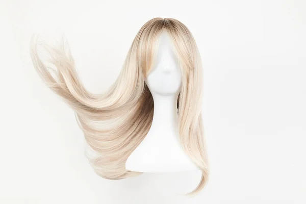 Natural looking blonde wig on white mannequin head. Long hair on the plastic wig holder isolated on white background, front vie
