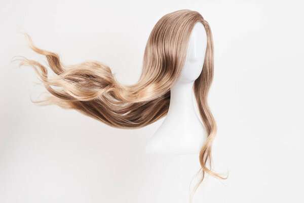 Natural looking blonde wig on white mannequin head. Long hair on the plastic wig holder isolated on white backgroun