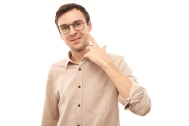 Genç erkek portresi beyaz stüdyo arka planında izole edilmiş gözlük parmağıyla işaret ediyor. Görüş kontrolü ve görme kaybı konsepti, gözlük dükkanı