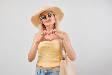 50 'li yaşların kadınının portresi hava öpücüğü gönderiyor. Beyaz stüdyoda izole edilmiş kalp şeklinde el ele.