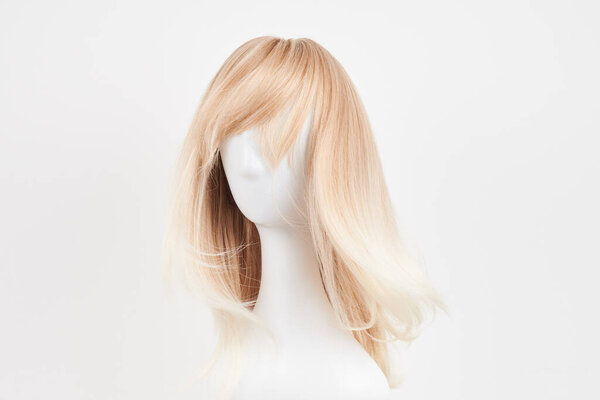 Естественно выглядящий светлый парик на голове белого манекена. Длинные волосы на пластиковом держателе парика изолированы на белой спинке