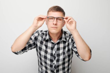 Gözlüklü genç erkek portresi, beyaz stüdyo arka planında izole edilmiş kameraya bakıyor. Görüş kontrolü ve görüş kaybı, arama konsepti, gözlük dükkanı