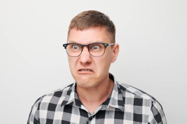 Beyaz stüdyo arka planında izole edilmiş öfkeli genç bir adamın portresi. Şeytan suratlı. İnsani duygular, yüz ifadesi kavramı