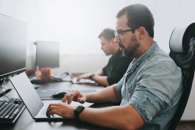 Çeşitli ofislerde bilgisayar üzerinde çalışan iki profesyonel erkek programcının portresi. Modern bilişim teknolojileri, yapay zekanın geliştirilmesi, programlar, uygulamalar ve video oyunları konsepti