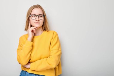 Gözlüklü zeki sarışın kız çenesine dokunuyor, beyaz stüdyo arka planında fotokopi çekmeyi seçiyor. Kendine güvenen zeki dahi.