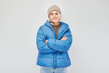 Beyaz stüdyo arka planında neşeli bir şekilde izole edilmiş beyaz sarışın bir kadının portresi. Kışın mavi ceketli, şapkalı, neşeli yüzlü mutlu kız.