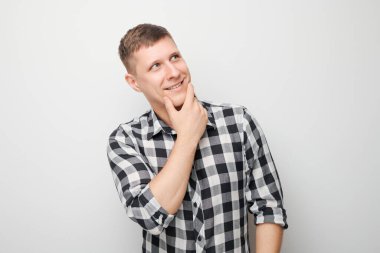 Çeneye dokunan tişörtlü zeki bir adamın portresi şüphelerin beyaz stüdyo arka planında kopya alanı ile izole edildiğini düşünüyor.