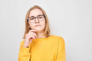 Gözlüklü zeki sarışın kız çenesine dokunuyor, beyaz stüdyo arka planında fotokopi çekmeyi seçiyor. Kendine güvenen zeki dahi.