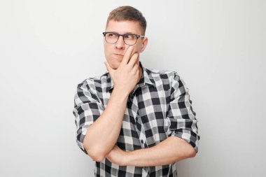 Çeneye dokunan tişörtlü zeki bir adamın portresi şüphelerin beyaz stüdyo arka planında kopya alanı ile izole edildiğini düşünüyor.