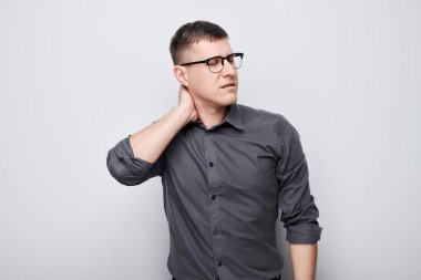Portrait of young man suffering from pain, touching neck isolated on white studio background. Psychosomatics of stress, degenerative disease of spine clipart