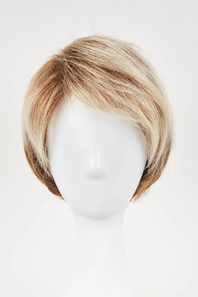 Natural looking blonde fair wig on white mannequin head. Short hair cut on the plastic wig holder isolated on white background, front vie
