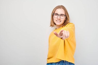Kendine güvenen öğrenci portresi beyaz stüdyo arka planında izole edilmiş kamerayı işaret ediyor. Hoş geldin jesti, takım konseptimize katıl.