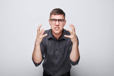 Beyaz stüdyo arka planında izole edilmiş öfkeli bir şekilde el ele tutuşan öfkeli genç adamın portresi. Şeytan patron suratı. İnsani duygular, yüz ifadesi kavramı