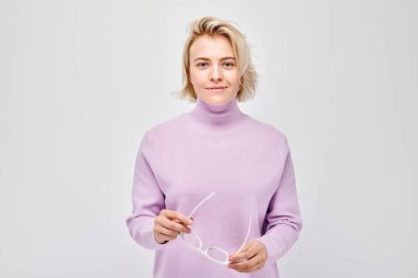 Beyaz stüdyo arka planında neşeli bir şekilde izole edilmiş beyaz sarışın bir kadının portresi. Leylak süveter ve gülen yüzlü gözlüklü mutlu kız.