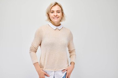 Beyaz stüdyo arka planında neşeli bir şekilde izole edilmiş beyaz sarışın bir kadının portresi. Mutlu kız bej bluzlu, gülen surat ifadeli.