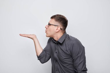 Genç adamın hava öpücüğü gönderen portresi, avucunda bir şey tutan, beyaz stüdyo arka planında izole edilmiş ürünü gösteren.