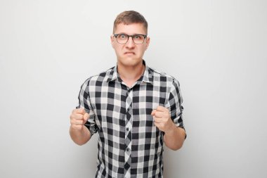 Beyaz stüdyo arka planında izole edilmiş yumruklarını sıkan öfkeli genç adamın portresi. Şeytan suratlı. İnsani duygular, yüz ifadesi kavramı