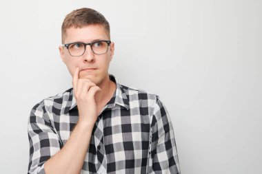 Çeneye dokunan tişörtlü zeki bir adamın portresi şüphelerin beyaz stüdyo arka planında kopya alanı ile izole edildiğini düşünüyor.