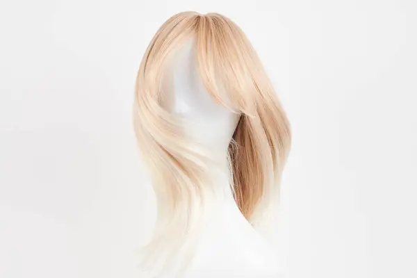 Natural looking blonde wig on white mannequin head. Long hair on the plastic wig holder isolated on white background, front vie