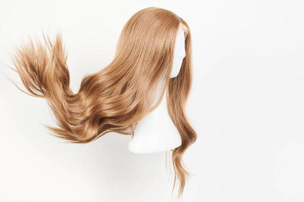 Естественно выглядящий темно-блондинистый парик на белой голове манекена. Длинные светлые волосы подстрижены на пластиковом держателе парик изолированы на белом фоне