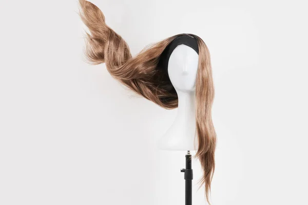 Natural looking dark blonde wig on white mannequin head. Long fair hair cut on the plastic wig holder isolated on white background