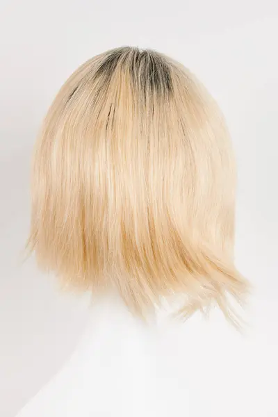 Natural looking blonde fair wig on white mannequin head. Short hair cut on the plastic wig holder isolated on white background, back vie