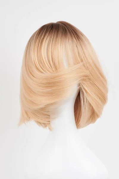Natural looking blonde fair wig on white mannequin head. Short hair cut on the plastic wig holder isolated on white backgroun