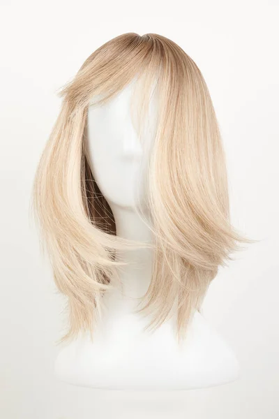 Natural looking blonde fair wig on white mannequin head. Middle length hair cut on the plastic wig holder isolated on white background, front vie