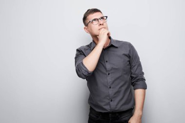 Çeneye dokunan tişörtlü zeki bir adamın portresi şüphelerin beyaz stüdyo arka planında kopya alanı ile izole edildiğini düşünüyor.