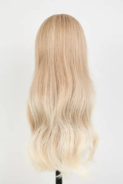 Natural looking blonde wig on white mannequin head. Long hair on the plastic wig holder isolated on white background, back vie