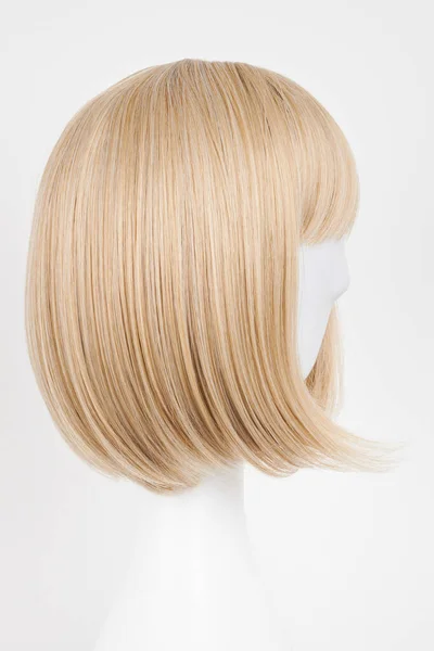 Natural looking blonde fair wig on white mannequin head. Short hair cut on the plastic wig holder isolated on white background, side vie