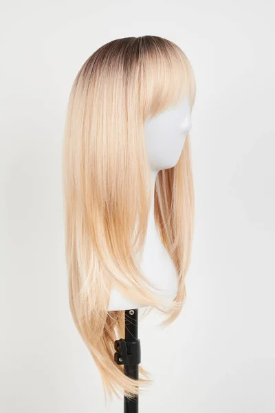 Natural looking blonde wig on white mannequin head. Long hair on the plastic wig holder isolated on white backgroun