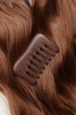 Kahverengi saç bukleleri ve beyaz arka planda ahşap bir tarak, saç bakımı, güzellik salonu konsepti