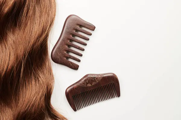 Curls of brown hair and a wooden comb on a white background, hair care, beauty salon concept