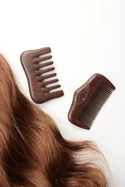 Curls of brown hair and a wooden comb on a white background, hair care, beauty salon concept