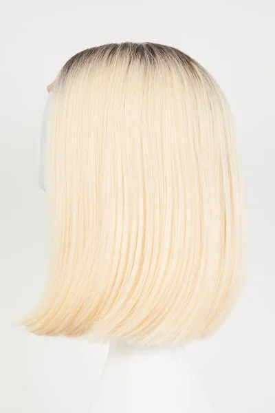 Natural looking blonde fair wig on white mannequin head. Middle length hair cut on the plastic wig holder isolated on white background, side vie