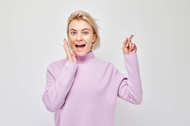 Genç, sarışın bir kadın, gösterişsiz bir şekilde işaret ediyor. Beyaz stüdyo arka grubunda boş bir alan ya da mesaj gösteriyor.