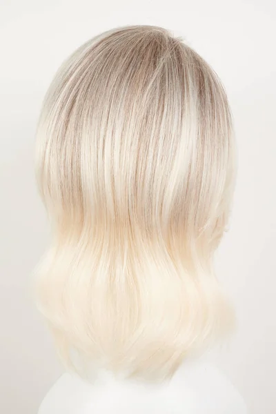 Natural looking blonde fair wig on white mannequin head. Middle length hair cut on the plastic wig holder isolated on white background, back view